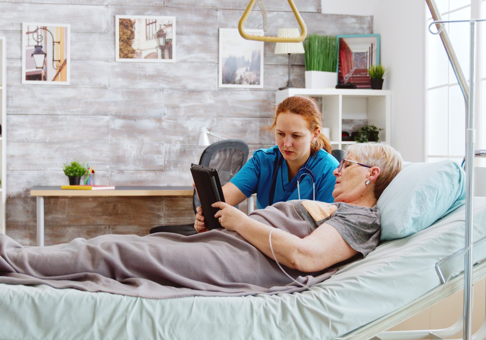 female-caregiver-helps-old-disabled-woman-lying-hospital-bed-use-digital-tablet-pc-bright-room-with-big-windows